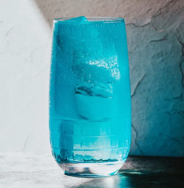 Glass of vibrant blue AMF cocktail with a lemon twist garnish