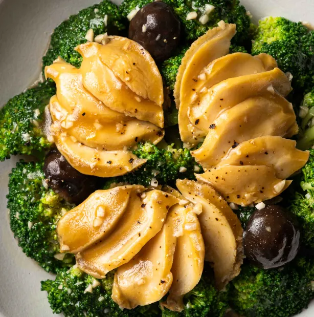 Braised abalone and broccoli dish garnished with sesame seeds and herbs.