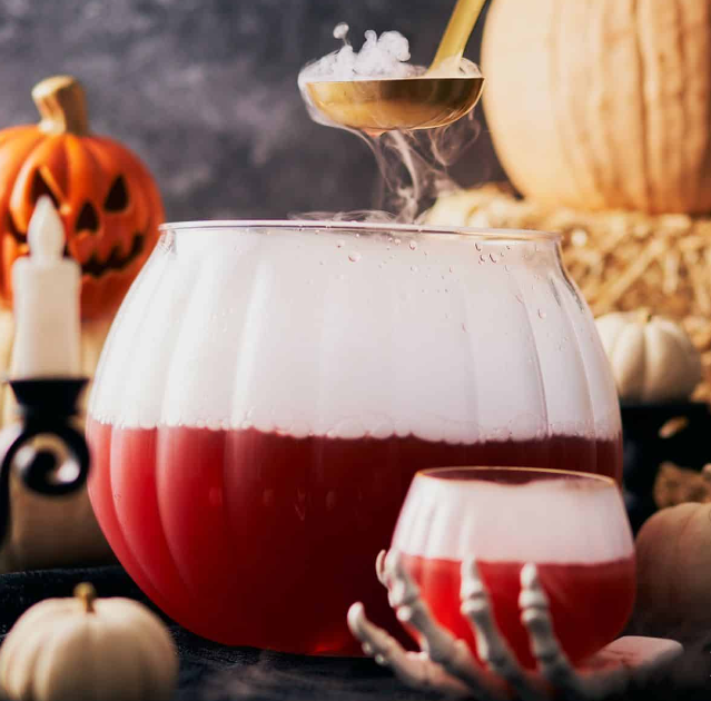 A vibrant Halloween punch bowl filled with a crimson-colored beverage, garnished with floating orange slices, and surrounded by autumn leaves and spooky decorations.