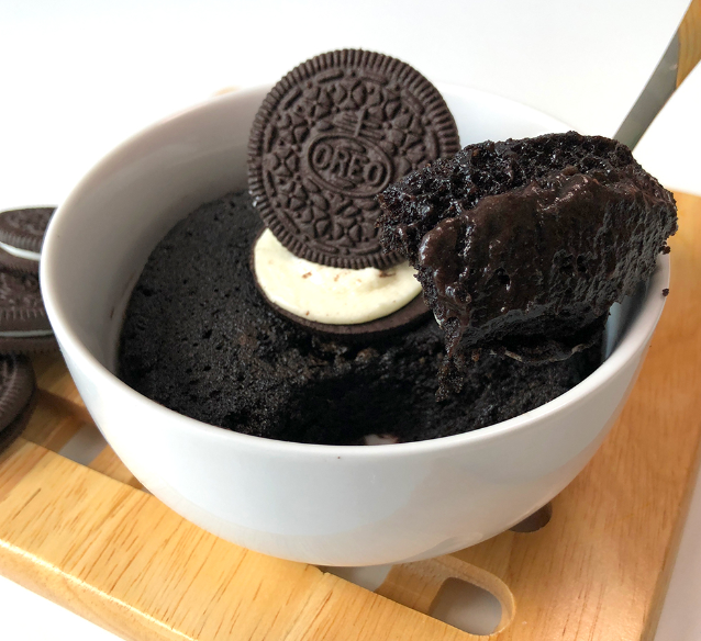 A delicious Oreo mug cake topped with whipped cream and a sprinkle of crushed Oreo cookies, served in a white ceramic mug.