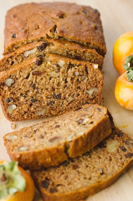 Sliced persimmon bread on a wooden board with fresh persimmons on the side