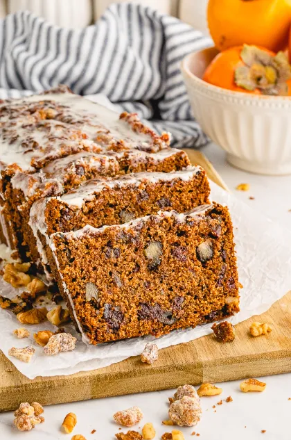 Sliced persimmon bread on a wooden board with fresh persimmons on the side