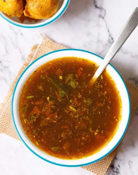 A bowl of aromatic rasam garnished with fresh coriander leaves